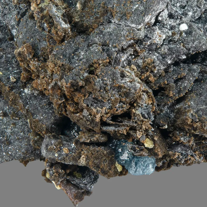 Gerdtremmelite: Intergrown spherules (to 0.3 mm) of brown gerdtremmelite on a siliceous breccia, with blue scorodite and tiny rosettes of yellow powellite. 26 mm field of view. MGMH Collection 2020.7.709.